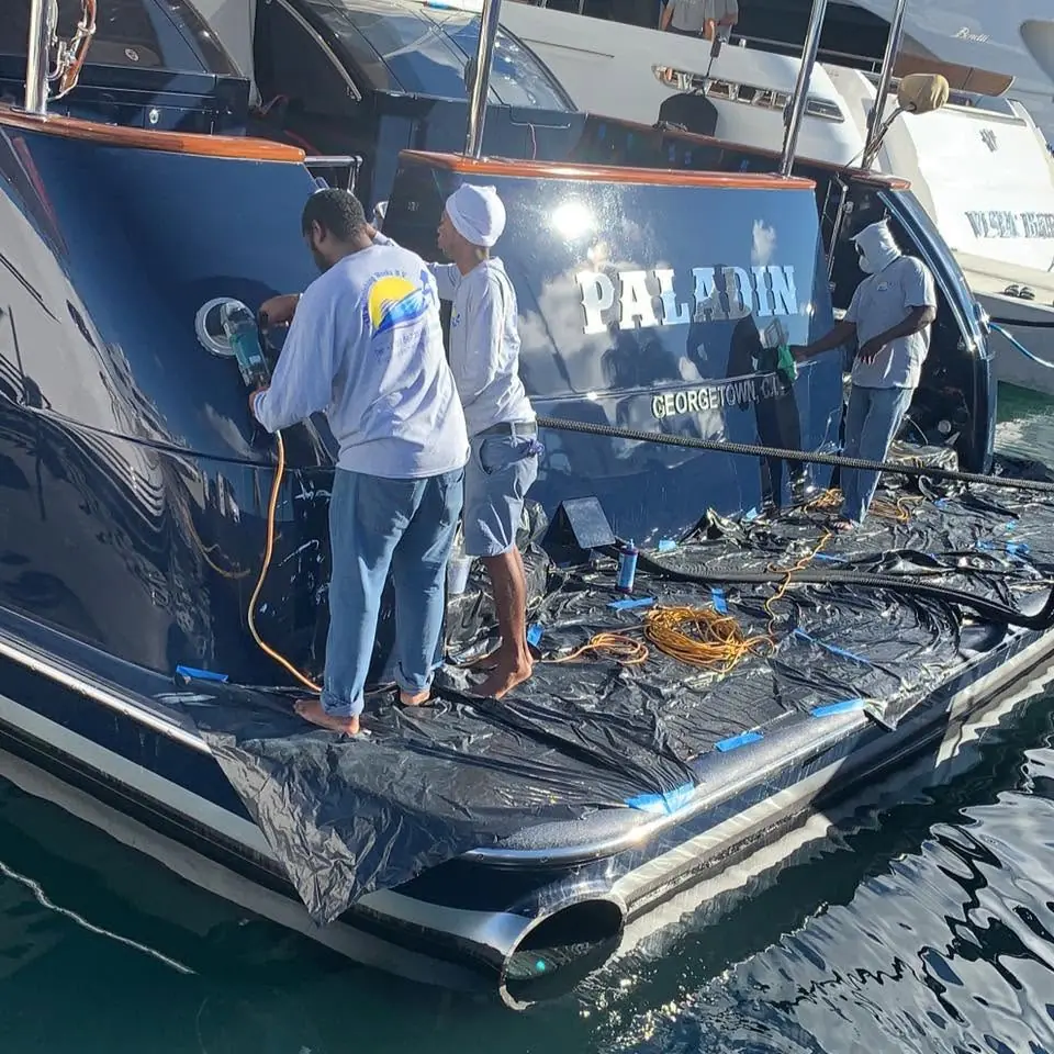 Technicians spray-painting a luxury yacht hull in a St. Maarten boatyard